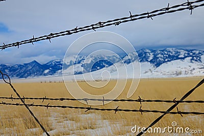 CLOSE UP: Rusty barbed wire fence runs around a pasture under the snowy Rockies Stock Photo