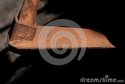 Close up of a rusty spade hovering above the ground from above. The background is light and shadow. The handle is made of wood Stock Photo