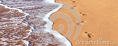 Close-up of the sea coast clear sea water washes a smooth brown sandy beach and footprints of bare human feet Stock Photo