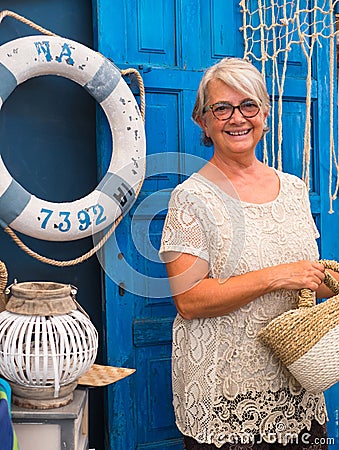 Close up of senior pretty lady with gray hair looking at camera. Romantic and rustic corner with blue door. Navy style accessories Stock Photo