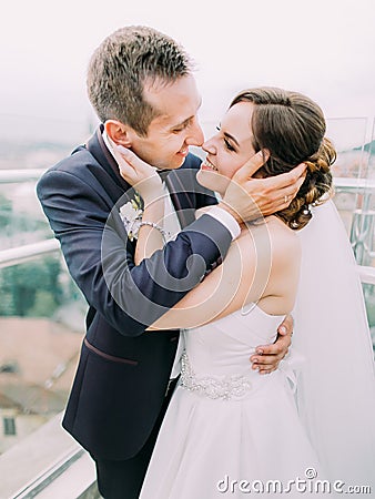 The close-up sensitive portrait of the happy newlyweds touching the faces of each other. Stock Photo