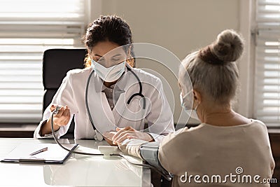 Close up doctor wearing mask measuring old woman blood pressure Stock Photo