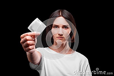 Close-up of a serious young woman showing a packed condom on a black background. Healthy lifestyle concept. Copy space. Stock Photo