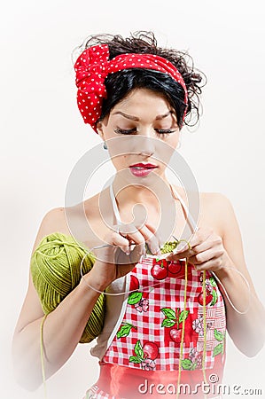 Close up on young brunette lady having fun wearing apron and red bow and doing knitting Stock Photo