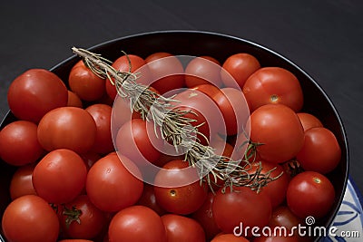 Close up shot of a bowl containing fresh, red tomatoes and a branch of fragrant rosemary Stock Photo