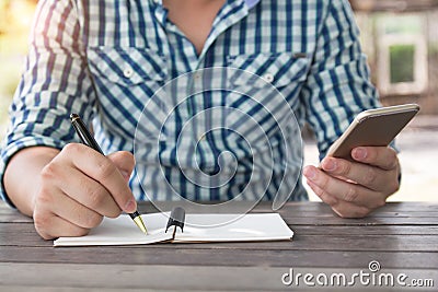 Close up shot business man taking down note writing with ballpoint pen holding, using mobile smart phone in other hand working in Stock Photo