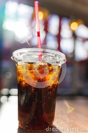 Close up shot of cold refreshing cola drink with ice and bubbles in plastic glass with red straw on wooden table with sun flare Stock Photo