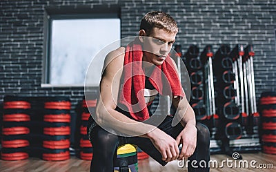Close-up shot of handsome fit man relaxing after exercises with red towel on neck in the gym. Tired athletic male rest after hard Stock Photo