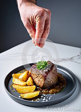 Close up shot of a man's hand pouring salt on a sirloin steak dish. AI generated Stock Photo