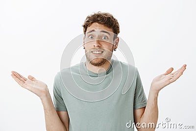 Close-up shot of questioned awkward handsome male in earrings, shrugging and spreading palms cluelessly, being unaware Stock Photo