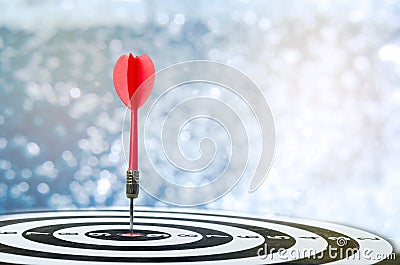 Close up shot red dart arrow on center of dartboard over bokeh b Stock Photo
