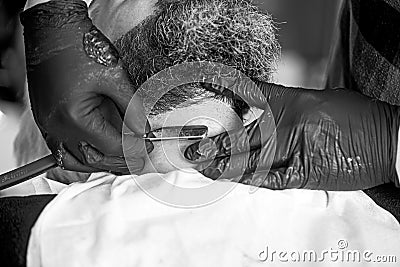 Close-up side view of young bearded man getting beard haircut by hairdresser at barbershop. Getting perfect shape. Stock Photo