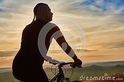 Close-up of silhouette of cyclist standing with bike against beautiful sunset. Stock Photo