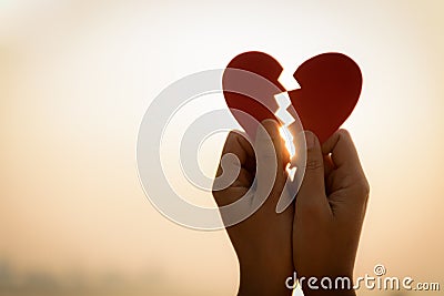 Close up and Silhouette of Woman hand holding broken paper red heart on sunset. Stock Photo