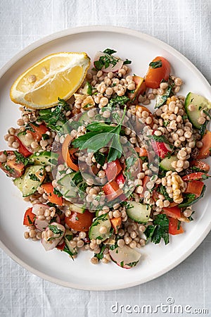 Close-up of a single plate of a healthy vegan wholewheat pearl couscous salad on white plate and white background, flatlay Stock Photo