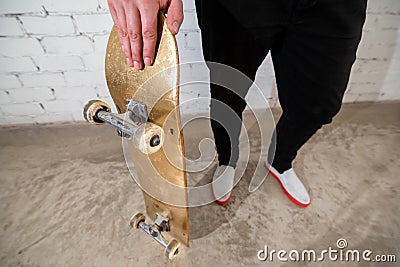 Close up of skateboarder standing next to a white brick wall. Athletic teenager wearing jeans with a skateboard. Urban style, Stock Photo