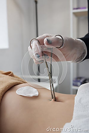 Close up of skin held in piercing tool as needle is ready to go in to pierce naval. Stock Photo