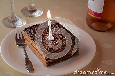 Slice of a layered chocolate cake with one candle and two glasses and bottle of wine Stock Photo