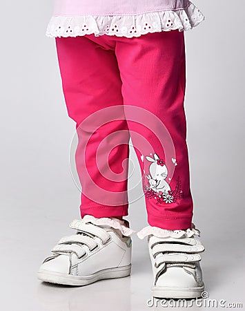 Close-up of small baby girl in pink stylish casual pants with ruffles and print bunnies and white sneakers Stock Photo