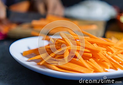 Pile of thin carrot slices on white plate with blurry background Stock Photo