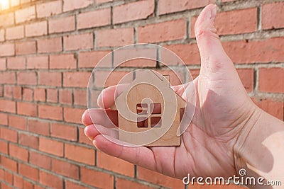 Close-up of a small wooden house in hand against a brick wall background. Concept - security, purchase, construction of real Stock Photo
