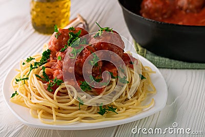 Close-up of spaghetti with meatballs with tomato sauce and parsley in white plate and black pan with meatballs Stock Photo