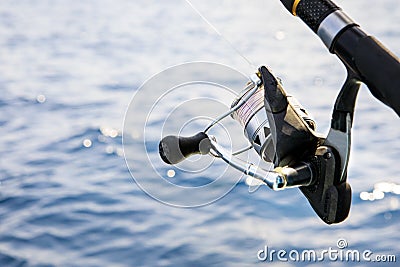 Close up spinning fishing rod against blue sea watger background Stock Photo