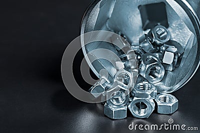 Small hex nuts spilled on heap in big socket for ratchet wrench with reflection on black background Stock Photo