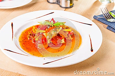 Close up stew fish fillet with vegetables decorated with basil leaf on the white plate on the served woodan table. healthy food, Stock Photo