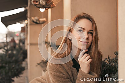 Close-up street portrait of a young girl wearing a coat, on the background of a beige wall, looks up and thinks. Street photo of a Stock Photo