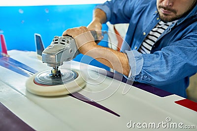 Tanned man polishing surfing board in workshop Stock Photo