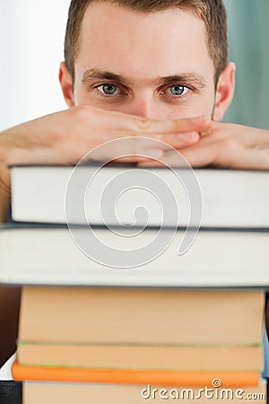 Close up of student hiding behind a pile of books Stock Photo