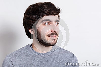 A close-up of stylish hipster with trendy beard and hairstyle, dark big eyes dressed in casual clothes looking happily aside. Port Stock Photo