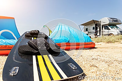 Close-up surf board and kite equipment on sand beach shore watersport spot on bright sunny day against rv camper van Stock Photo