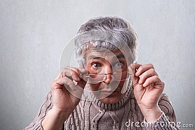 A close-up of surprised adult with gray hair and wrinkles wearing glasses. A senior man touching his eyeglasses looking with wide Stock Photo