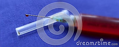 Close-up of a syringe with cannula and drop in front of dark blue background Stock Photo