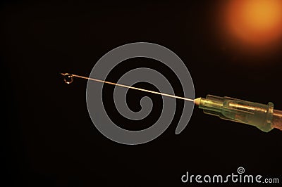 Close-up of a syringe with cannula and drop in front of dark red background Stock Photo