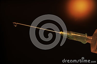 Close-up of a syringe with cannula and drop in front of dark red background Stock Photo