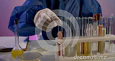Close-up of a table with test tubes in a stand. a person in blue protective clothing and white gloves examines the Stock Photo