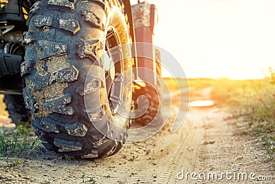 Close-up tail view of ATV quad bike on dirt country road at evening sunset time. Dirty wheel of AWD all-terrain vehicle. Travel Stock Photo