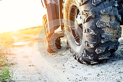 Close-up tail view of ATV quad bike on dirt country road at evening sunset time. Dirty wheel of AWD all-terrain vehicle. Travel Stock Photo