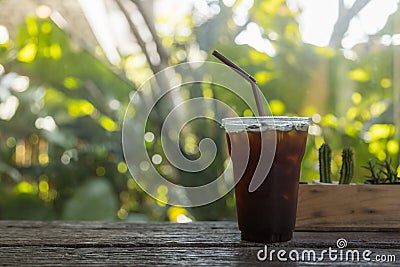 Close up of take away plastic cup of iced black coffee Americano under sunlight on wooden table in garden with green leaf nature Stock Photo