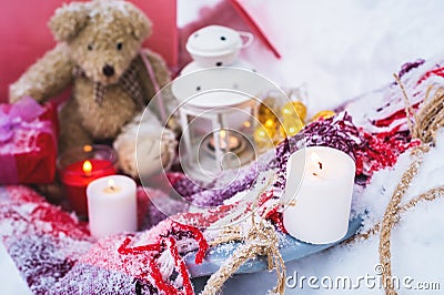 A close-up of a teddy bear with Christmas candles on a cozy checkered plaid outdoors next to a red gift box sprinkled Stock Photo