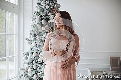 Close-up tenderness female hand hugging pregnant tummy feeling fondness at Christmas tree Stock Photo