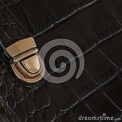 Close-up texture of black handbag from genuine leather with embossed under the skin of reptile, gold lock. With place Stock Photo