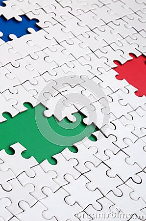 Close-up texture of a white jigsaw puzzle in assembled condition with missing elements, under which surfaces of different colors Stock Photo