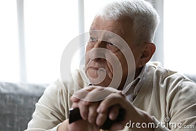 Close up thoughtful sad older man folded hands on cane Stock Photo