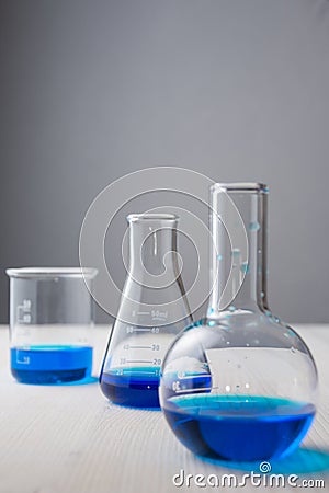 Close-up of three test tubes with blue liquid and selective focus on white wooden table and gray background in vertical Stock Photo