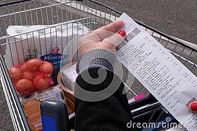 Close up of a till receipt from a French supermarket with a supermarket trolley full of purchases in the background Editorial Stock Photo