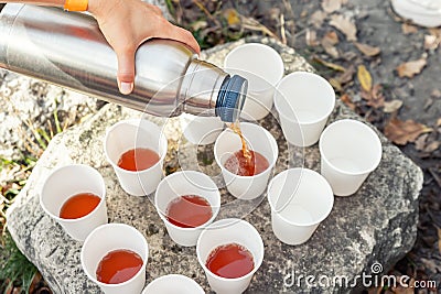 Close-up top above view woman hand hold steel thermos pouring hot tea many white paper cup group picnic mountain Stock Photo